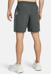 Šedé sportovní šortky s texturovanou tkaninou, elastickým pasem a zeleným logem po straně. Jsou nošeny bílé sportovní boty.