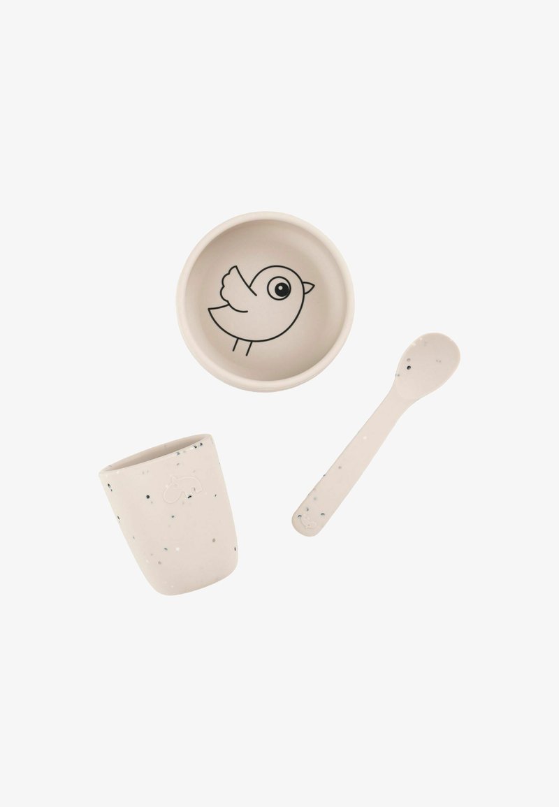 Juego de tres elementos de mesa: un bol con un gráfico de un pájaro, una taza con textura moteada y una cuchara a juego, todo en tonos beige suaves.