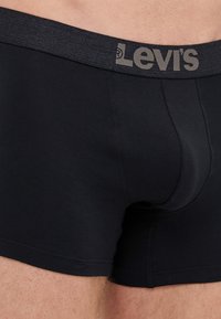 Svarta bomullsboxer med en grå elastisk midja som har "Levi's"-logotypen. Slät textur och åtsittande design.