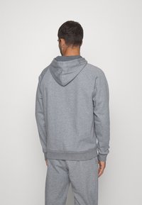 Felpa grigia con tasca a marsupio, polsini e orlo a costine, realizzata in tessuto morbido, con cappuccio regolabile e maniche raglan.