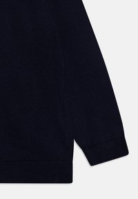 Navy stickad tröja i närbild som visar ribbade manschetter och nederkant, slät textur och en åtsittande design.