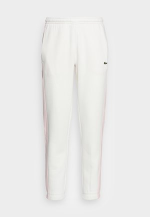 Bílé sportovní joggingové kalhoty s bledě růžovými bočními pruhy, elastickým pasem a malým zeleným logem krokodýla na pravém stehně.