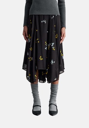 Black skirt with a flowing, asymmetrical hem, featuring a floral pattern in yellow, blue, and white. Paired with gray knitted socks and black shoes.