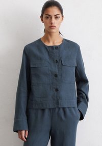 Donker teal cropped jasje van lichtgewicht stof, met een ronde halslijn, lange mouwen, twee borstzakken en ronde knopen.