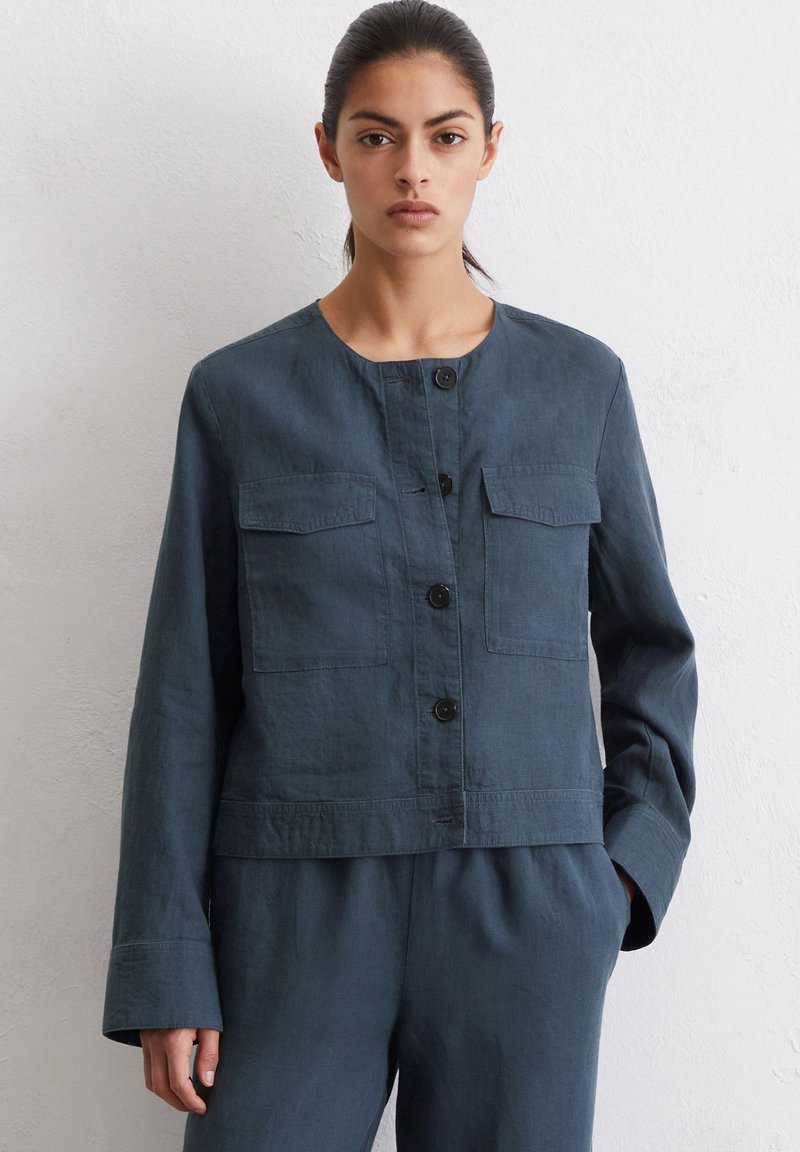 Donker teal cropped jasje van lichtgewicht stof, met een ronde halslijn, lange mouwen, twee borstzakken en ronde knopen.
