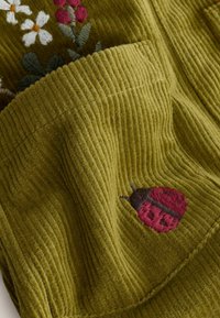 Olivengrüner Cordstoff mit floralem Stickmuster und einem roten Marienkäfer-Design. Strukturiert Oberfläche mit vertikalen Rippungen.