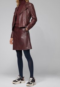 Burgundy läder-motokappa, matchande kjol, marinblå strumpbyxor och svarta chunky sneakers med vita och röda detaljer. Slät textur och formsydd design.