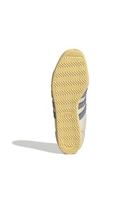 Suola di sneaker beige Adidas con motivo a spina di pesce e tre strisce grigio scuro di lato, che proietta un'ombra su sfondo bianco.