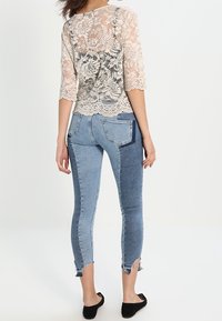 Top in pizzo con maniche a tre quarti e motivo floreale beige. Jeans skinny con design a blocchi di colore in denim azzurro chiaro e scuro.