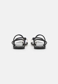 Svarta platta sandaler med tunna remmar och platt sula, med en slät yta och minimal design. Ingen synlig logotyp.