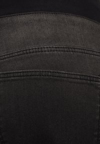 Tecido de denim preto com uma textura suave, apresentando costuras e bolsos contrastantes. O tecido possui um leve acabamento brilhante.