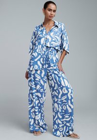 Ensemble en lin rayé bleu et blanc comprenant une chemise ample à boutons et un pantalon large. Présente une coupe décontractée et une texture naturelle.