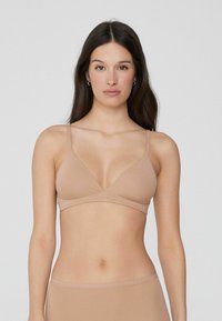 Bralette beige clair, sans rembourrage, avec un design en V, des bretelles minces et ajustables, et une texture lisse et extensible. Construction simple et sans couture.