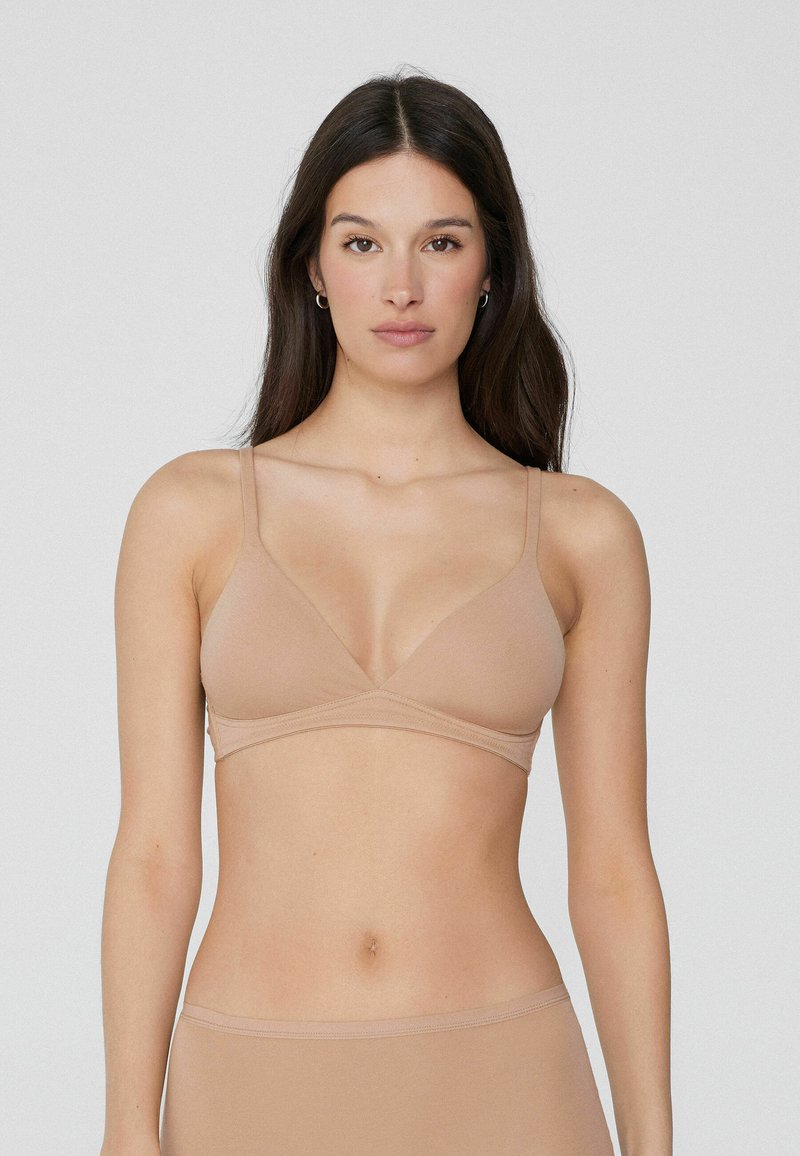 Bralette beige clair, sans rembourrage, avec un design en V, des bretelles minces et ajustables, et une texture lisse et extensible. Construction simple et sans couture.