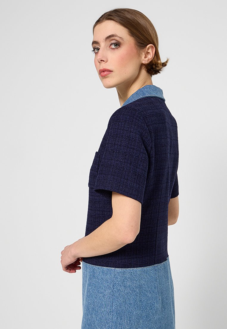 Marineblaues strukturiertes kurzärmliges Shirt mit hellblauem Kragen. Verfügt über eine Brusttasche und einen kontrastierenden blauen Jeansrock.