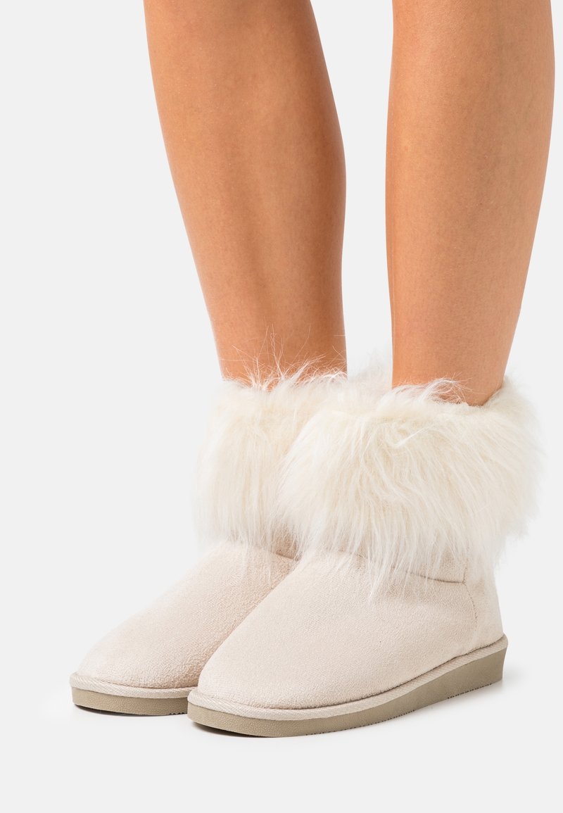 Beige Wildlederschuhe mit flauschigem weißen Kunstfellbesatz, flachen Gummisohlen, runden Zehen und nahtlosem Oberdesign.