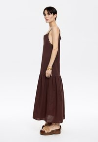 Abito marrone con top aderente e gonna svasata. Presenta un bordo scalloped lungo il collo. Abbinato a sandali con plateau con accenti testurizzati.
