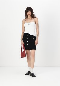 Hvit ribbet tanktopp med et lite grafisk print, kombinert med et svart miniskjørt med gullknapper og lommer. Fullført med en rød veske.