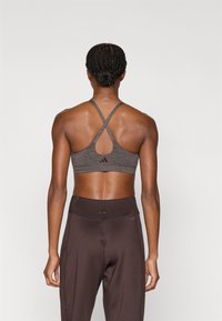 Γκρι αθλητικό σουτιέν με λουριά που διασταυρώνονται και σχέδιο με άνοιγμα στην πλάτη. Σετ με καφέ κολάν με ψηλή μέση, και τα δύο κατασκευασμένα από απαλό ύφασμα.