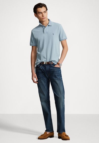 Gai zils polo krekls ar apkakli un mazu logo, apvienots ar tumši ziliem džinsiem. Modelis nēsā brūnus zamša mokasīnus un brūnu jostu.