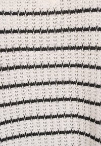 Pletený svetr s bílým základem a černými vodorovnými pruhy. Textura má otvorenou vazbu, která zvýrazňuje dekorativní vzorovaný design.