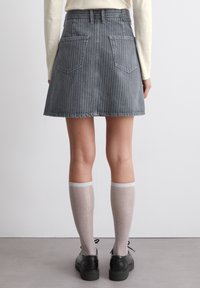 Mørk grå A-linjeet skjørt i denim med hvite vertikale striper, som har to baklommer. Kombinert med knelang, glitrende sokker og svarte sko.