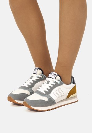 Witte en grijze sneakers met suède accenten in groen en mosterd, voorzien van een gestructureerde rubberen zool en witte veters.