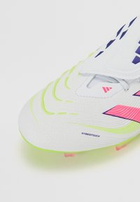 White football boot with textured surface, neon green accents, pink and purple details, and sleek design featuring a layered look.