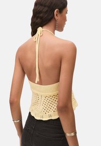 Top halter giallo lavorato a maglia con design a punto aperto, fascia a coste e chiusura con lacci. Abbinato a jeans neri a vita alta.
