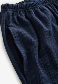 Pantaloni jogger texturați de culoare bleu marin, cu talie elastică și modele verticale în relief. Materialul pare moale și confortabil.