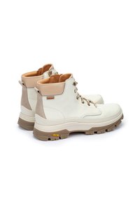 Botas de senderismo de cuero blanco con un acento de talón de ante beige, ojales dorados y suela Vibram. Características un diseño de cordones y un cuello acolchado.