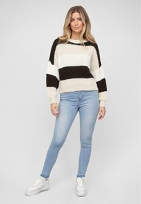 Gestreifter Pullover mit breiten schwarzen und cremefarbenen Streifen, lockere Passform und gerippte Bündchen. Kombiniert mit hellblauen Skinny Jeans und weißen Sneakers.