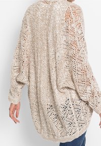 Cardigan beige a maglia aperta con un motivo in pizzo testurizzato e vestibilità oversize. Maniche larghe, polsini e orlo a costine.