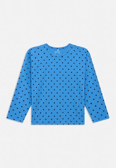 Blå langermet skjorte med svarte polkadotter, rund hals og rett kant, lagt flatt på hvit bakgrunn.