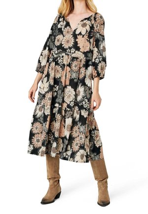 Mujer con vestido midi negro con grandes estampados florales en beige y blanco, mangas tres cuartos y botas de ante marrón hasta la rodilla.