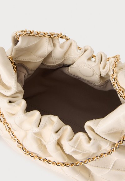 Sac à main en cuir froncé couleur crème avec une bandoulière chaîne dorée, montrant la doublure intérieure vide et sombre.