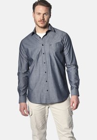 Dunkelblaues Hemd mit Knöpfen, mit einer Tasche, langen Ärmeln und schwarzen Knöpfen, aus glattem Stoff gefertigt. Kombiniert mit hellbeigen Cargo-Hosen.