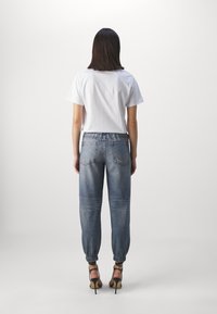 Witte katoen t-shirt, losse pasvorm. Blauwe denim joggerbroeken met elastische boorden en een lichte wassing. Zwarte gespenhakken. Eenvoudig ontwerp, casual uitstraling.