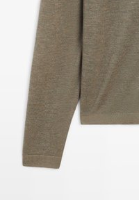 Grön stickad tröja med en mjuk textur, långa ärmar, ribbat nederkant och rak skärning. Tyget har en lätt lyster och ett subtilt mönster.