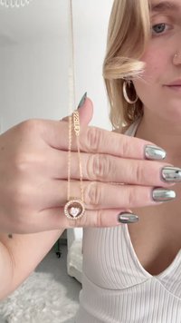 Guldhalsband med ett hjärtformat hänge, med en central rosa sten omgiven av små klara ädelstenar. Kedjan är smal och delikat.