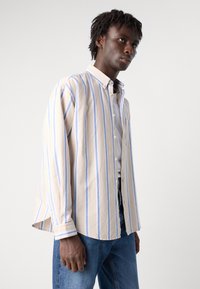 Gestreepte lange mouwen shirt in lichtbeige met verticale blauwe strepen. Met knoopsluiting, enkele zak en een ontspannen pasvorm met zijsplitten.