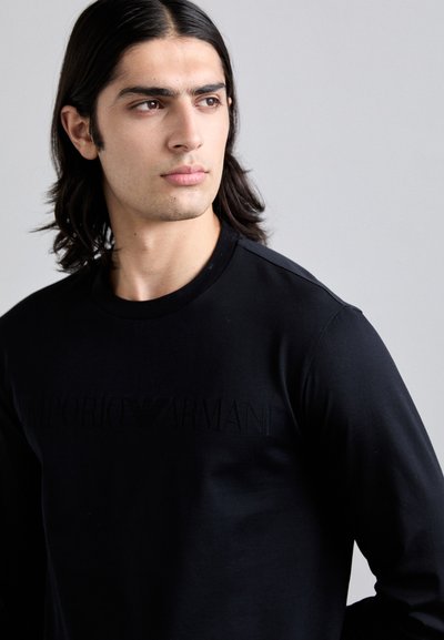 Camisa de manga longa preta com decote redondo e logótipo em relevo "Emporio Armani" no peito, feita de tecido suave com um design ajustado.
