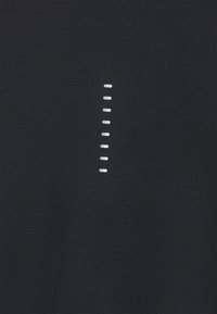 Svart tyg med en slät textur som har en vertikal rad av vita sydda detaljer i ett prickigt mönster ner i mitten.