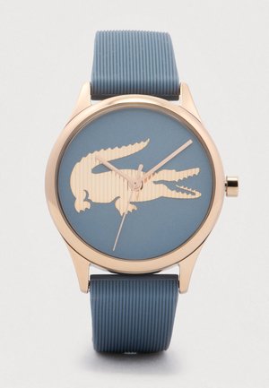 Round wristwatch with blue textured strap, gold bezel, and blue face featuring a large gold crocodile logo and gold hands.