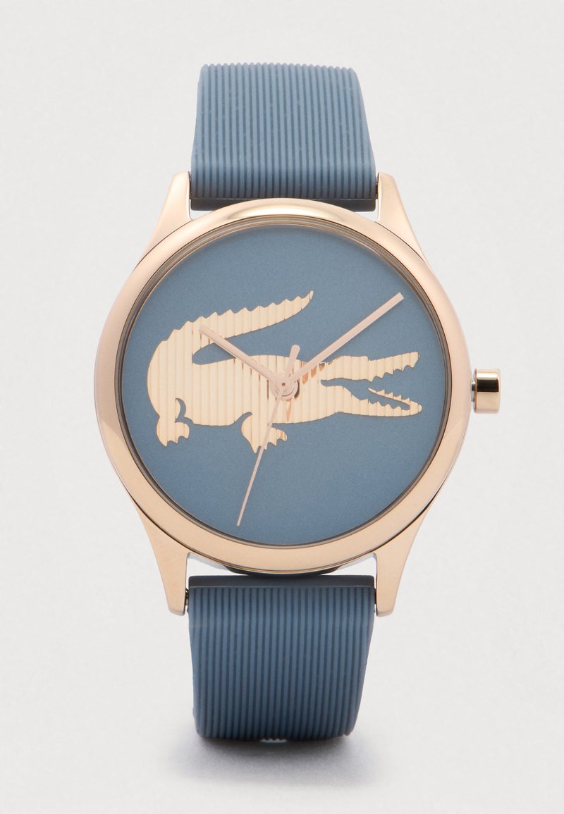 Round wristwatch with blue textured strap, gold bezel, and blue face featuring a large gold crocodile logo and gold hands.