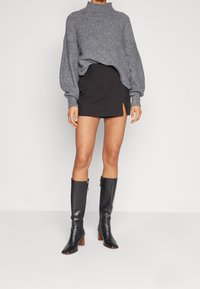 Pull en maille gris à col montant, assorti à une jupe mini noire avec une fente sur le côté. Bottes en cuir noir jusqu'aux genoux avec talons blocs.