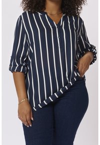 Blouse bleu marine avec des rayures blanches verticales, encolure en V, détail de boutons et manches retroussées. Confectionnée dans un tissu léger et lisse.