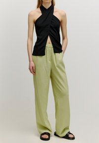 Haut halter noir avec texture plissée et détail découpé, associé à un pantalon large vert clair. Les chaussures comprennent des sandales plates noires.