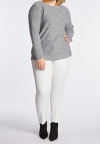 Šedý pletený svetr s kulatým výstřihem a texturovanou tkaninou, kombinovaný s bílými úzkými kalhotami a černými kotníkovými botami.