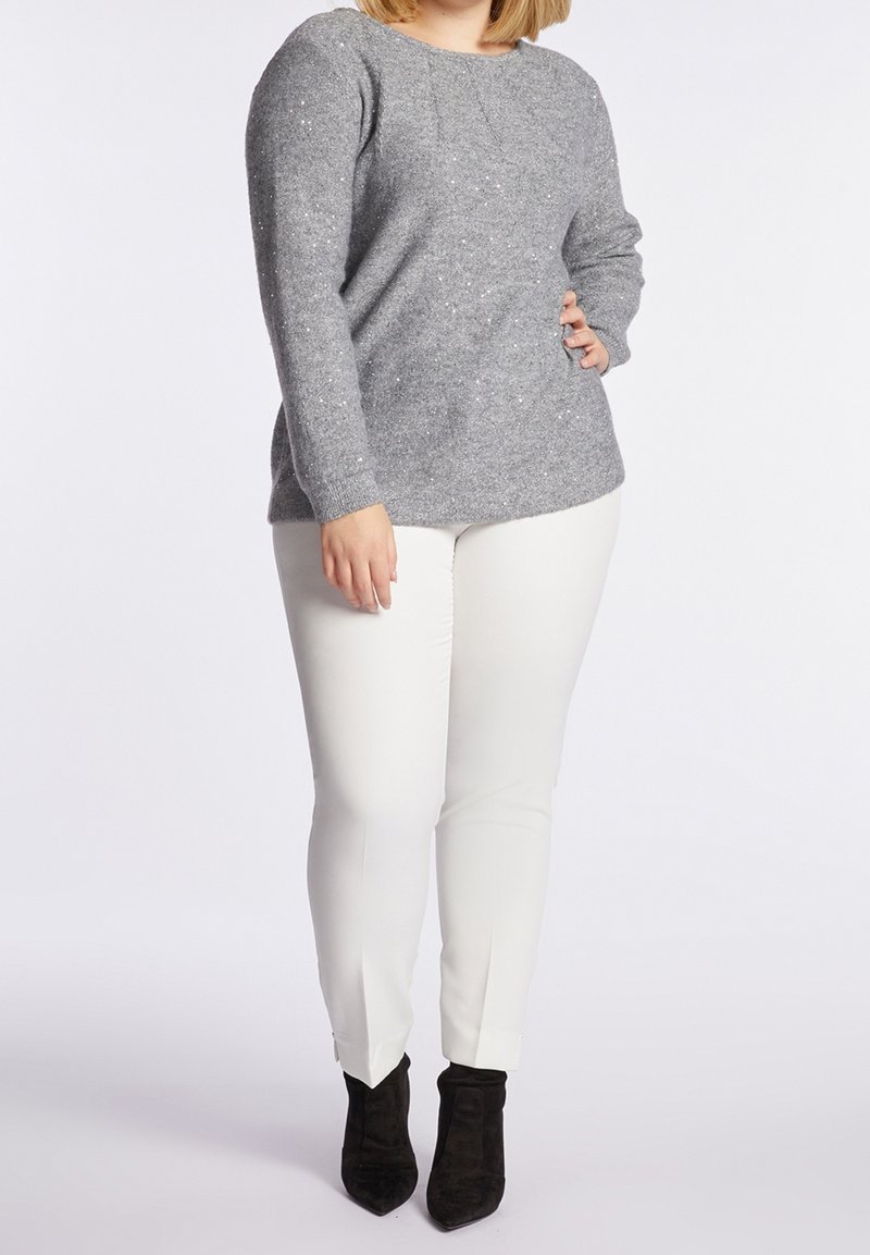 Šedý pletený svetr s kulatým výstřihem a texturovanou tkaninou, kombinovaný s bílými úzkými kalhotami a černými kotníkovými botami.